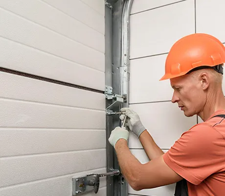 Technician wearing orange hard hat and gloves installing or maintaining a commercial sectional garage door.