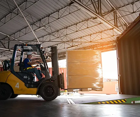 Forklift operating in a warehouse loading dock area with sunlight shining through an open door.