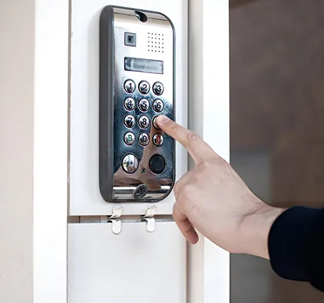 Person pressing a button on an electronic garage door keypad installed on an exterior wall for keyless access.