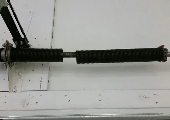 Rusty broken garage door torsion spring detached from door hardware on white wall