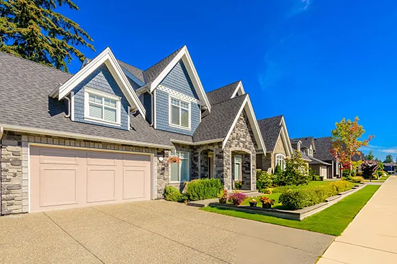 Grey house with two beige overhead garage doors under blue sky in Rowlett, TX