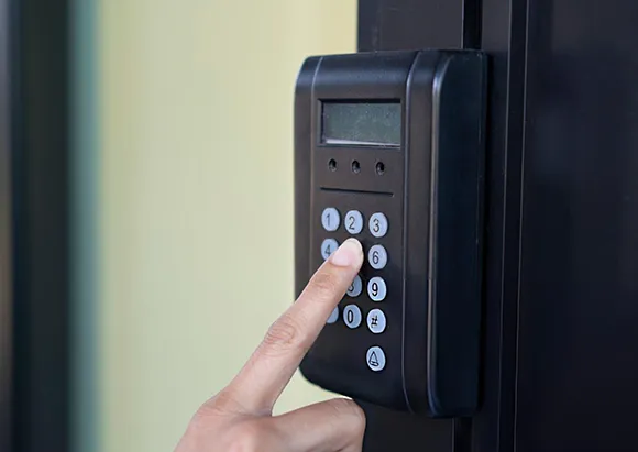 Finger pressing a button on a black digital garage door access keypad in Plano, TX.