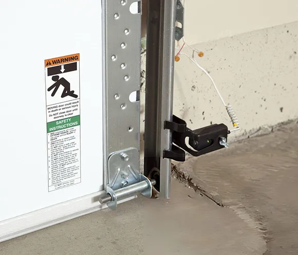 Close-up of a garage door photo-eye sensor mounted on a garage door track for safety detection.