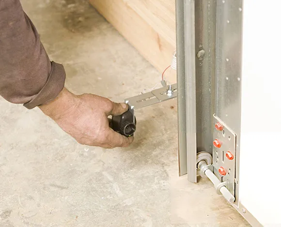 Technician hand working on installing or adjusting garage door sensor beam near garage door track.