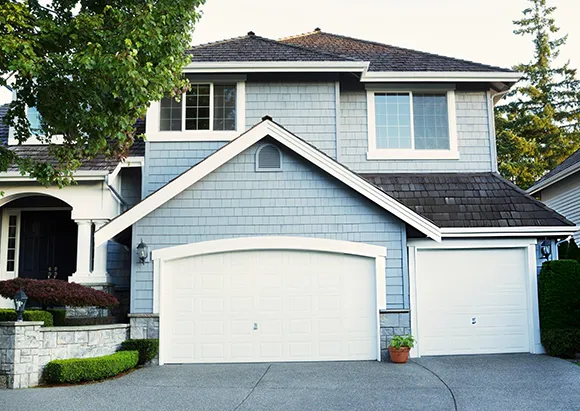 Two-story grey house with white panel garage door in suburban neighborhood in Plano, TX